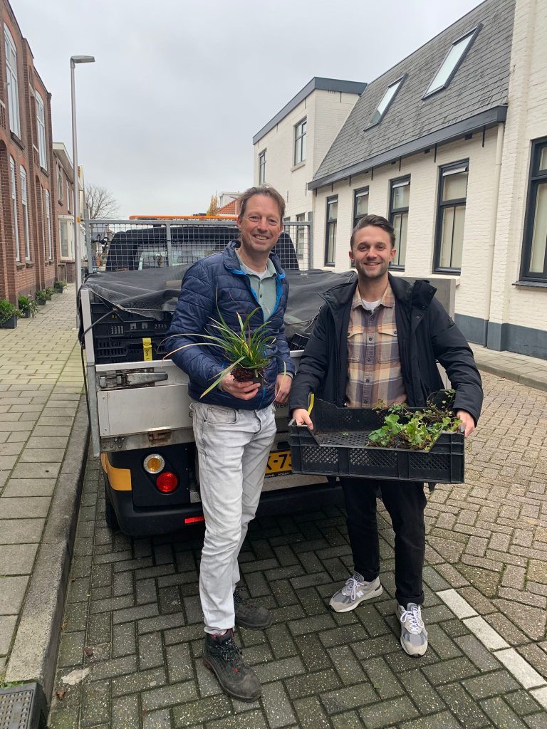 Twee mannen staan voor een wagen met planten in hun handen.